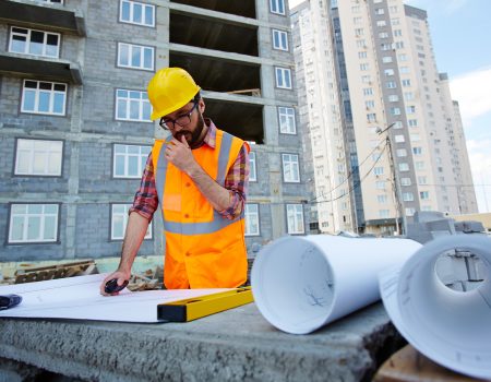Pensive worker in hardhat and uniform looking at sketch of new building