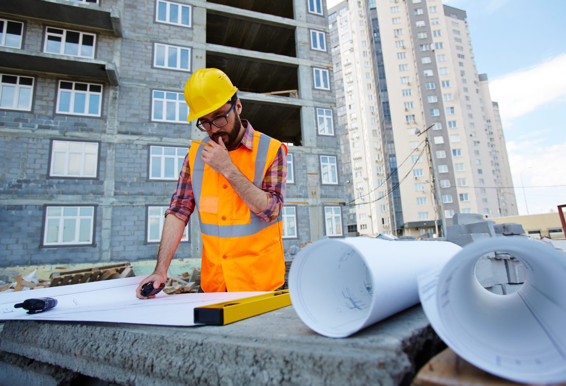 Pensive worker in hardhat and uniform looking at sketch of new building